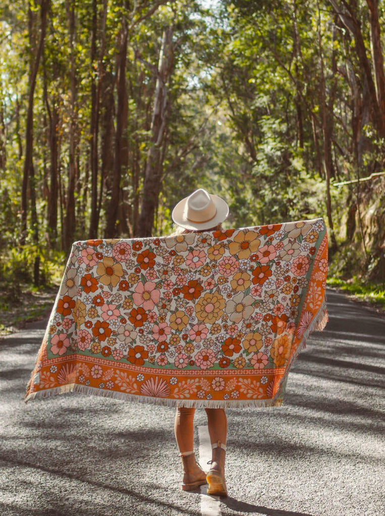 A person standing on a winding road in a forest, holding a Retro Floral Pattern Brown Throw Blanket over them to keep cosy while camping or living the vanlife